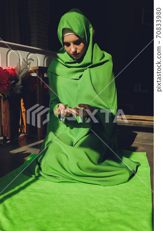 Muslim woman in hijab praying on mat indoors. 70833980