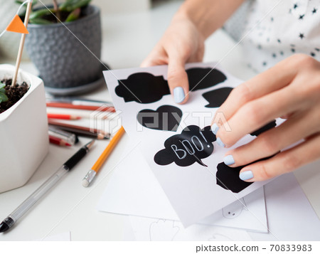 Woman writes Boo! on decorative black stickers for chalks. Handmade decorations for Halloween. Woman writes Boo! on decorative black stickers for chalks. Handmade decorations for Halloween. 70833983