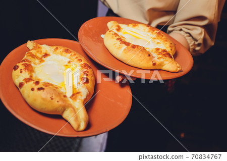 Homemade Ajarian Khachapuri with Sulguni Cheese Filled with a Raw Egg and Melted Butter Close Up. Fresh Hot Traditional Georgian Cheese-Filled Bread in the Form of a Boat. Homemade Ajarian Khachapuri with Sulguni Cheese Filled with a Raw Egg and Melted Butter Close Up. Fresh Hot Traditional Georgian Cheese-Filled Bread in the Form of a Boat. 70834767