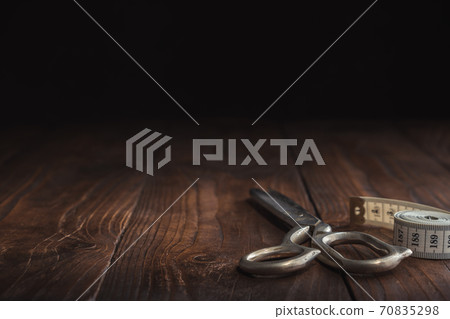 Sewing items - tailoring scissors and measuring tape on dark wooden table. Copy space for text. 70835298