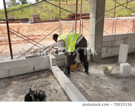 SEREMBAN, MALAYSIA -MARCH 16, 2020: Construction workers laying autoclaved aerated concrete block at the construction site. The use of this material can save time and facilitate construction work. SEREMBAN, MALAYSIA -MARCH 16, 2020: Construction workers laying autoclaved aerated concrete block at the construction site. The use of this material can save time and facilitate construction work. 70835316