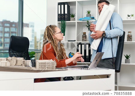 Serious female manager of design agency is upset as clumsy worker let out blueprints on her table. 70835888