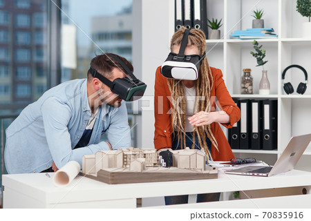 Two young architects in VR glasses working with layout of a residential area in modern office. 70835916