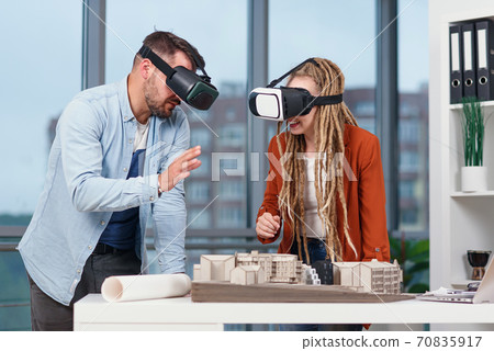 Two young architects in VR glasses working with layout of a residential area in modern office. 70835917