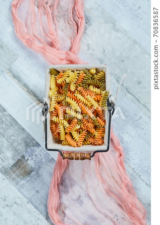Colorful uncooked pasta on a blue background with pink tablecloth 70836587