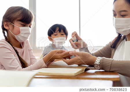 Young female teacher using an alcohol spray to disinfect student hands in classroom. Asian woman in face mask cleaning pupils' hands with hand sanitizer. School reopen after quarantine and lockdown 70838623
