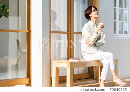 A woman spending her time drinking coffee on a garden bench on a sunny afternoon on a holiday 70840205