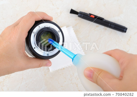 Hands blowing off dust from rear lens using silicone air blower. Hands blowing off dust from rear lens using silicone air blower. 70840282