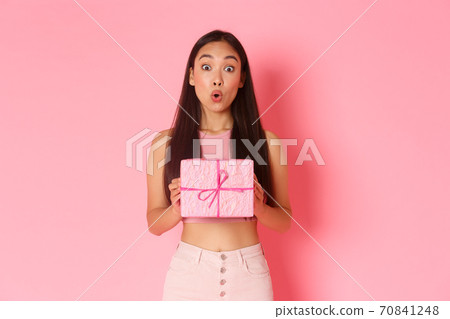 Holidays, celebration and lifestyle concept. Surprised and intrigued asian girl celebrating birthday receive wrapped gift, wonder what inside of present, standing amused over pink background 70841248