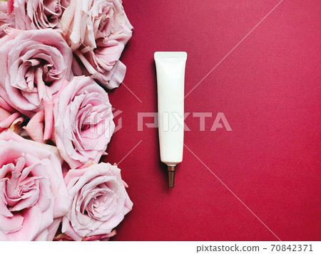 Mockup of white squeeze cosmetic tube with long nozzle and bronze screw cap and roses on red table. Bottle for branding. Top view, flat lay. Copy space. 70842371