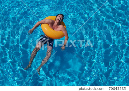 Orange circle and laughing guy in summer pool. Saturated blue water background. Summer holidays, laughter, joy of life and cheerful man. Pool party 70843285
