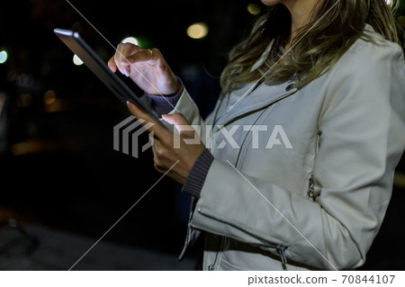 她的20多歲的年輕女子在晚上在公園裡使用平板電腦 70844107