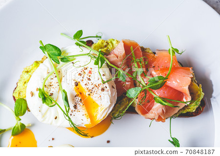 Toast with salmon, poached egg and avocado on white plate, top view. Poached egg with salmon and guacamole on rye bread. Toast with salmon, poached egg and avocado on white plate, top view. Poached egg with salmon and guacamole on rye bread. 70848187