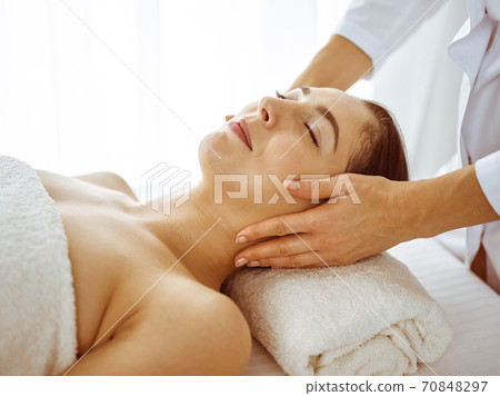 Beautiful brunette woman enjoying facial massage with closed eyes. Relaxing treatment in medicine and spa center concepts 70848297
