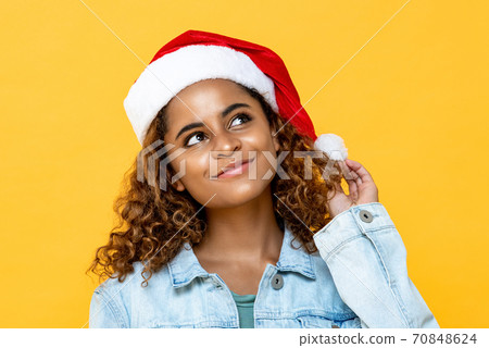 Pretty African American woman wearing Chritmas hat smiling and thinking Pretty African American woman wearing Chritmas hat smiling and thinking 70848624