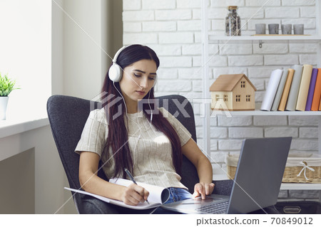 Woman in headphones and making notes during online lesson at home on laptop 70849012