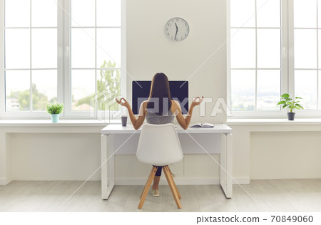 Woman taking break from work and meditating sitting at office table with computer and coffee 70849060
