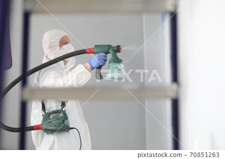 Man in protective suit and respirator sprays paint on walls. 70851263