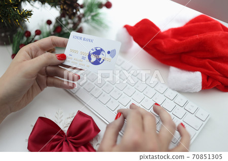 Female hands holding bank credit card near keyboard and santa claus hat and christmas tree. 70851305
