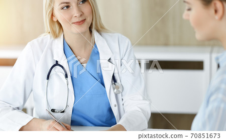 Woman-doctor and patient sitting and talking in sunny clinic. Blonde therapist is cheerfully smiling Woman-doctor and patient sitting and talking in sunny clinic. Blonde therapist is cheerfully smiling 70851673