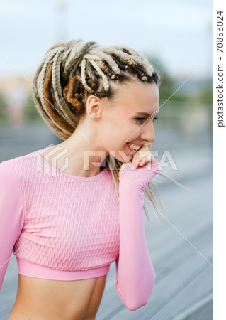 Summer urban portrait of a slender young beautiful woman with dreadlocks in a pink T-shirt and denim short shorts on a wooden staircase. 70853024