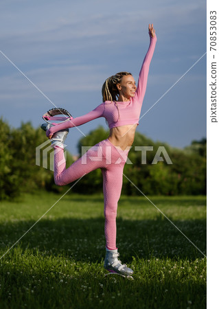 A young slender beautiful woman with dreadlocks in sportswear trains in the park outdoors. Kangoo jumps training. 70853083