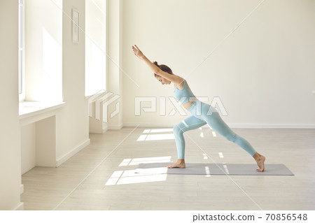 Serious young woman practicing balancing asana standing on rubber mat during yoga workout in gym 70856548