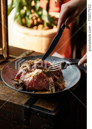 A female hand is preparing a vegetable salad with beef roast beef. A plate of salad with beef roast beef, onions, arugula, pepper and tomatoes on a black table. Top view. 70857932