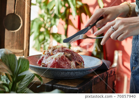 A female hand is preparing a vegetable salad with beef roast beef. A plate of salad with beef roast beef, onions, arugula, pepper and tomatoes on a black table. Top view. 70857940