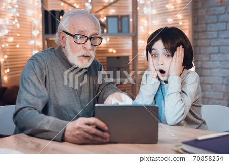 Gray haired grandfather holds a tablet.  70858254