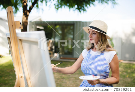 Portrait of mature woman with pallete painting outdoors in garden. Portrait of mature woman with pallete painting outdoors in garden. 70859291