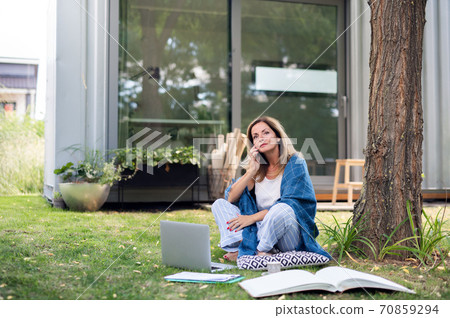 Mature woman in pajamas working in home office outdoors in garden, using smartphone. Mature woman in pajamas working in home office outdoors in garden, using smartphone. 70859294