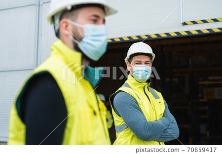 Men workers with face mask standing in front of warehouse, coronavirus concept. Men workers with face mask standing in front of warehouse, coronavirus concept. 70859417