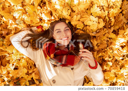 Gorgeous young woman lying among yellow autumn leaves, looking at camera and smiling, top view Gorgeous young woman lying among yellow autumn leaves, looking at camera and smiling, top view 70859418