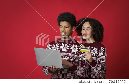 Smiling couple in sweaters buying gifts for family, african american young man with laptop and lady with credit card Smiling couple in sweaters buying gifts for family, african american young man with laptop and lady with credit card 70859622