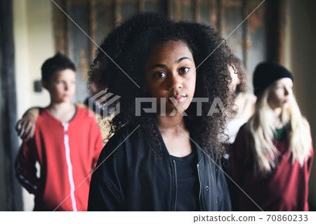 Portrait of mixed-race teenager girl with friends standing indoors in abandoned building. Portrait of mixed-race teenager girl with friends standing indoors in abandoned building. 70860233