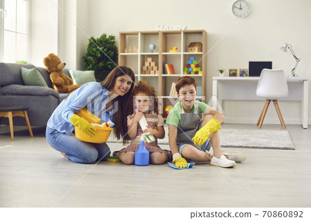 Happy mother and children in household gloves sitting on floor and looking at camera Happy mother and children in household gloves sitting on floor and looking at camera 70860892