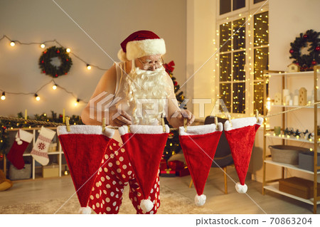 Santa Claus hanging his hats to dry on clothes line after doing laundry on winter holidays Santa Claus hanging his hats to dry on clothes line after doing laundry on winter holidays 70863204