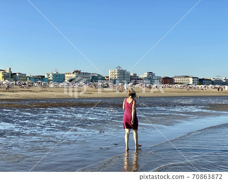 A middle aged woman is walking along the beach in the late afternoon on Caorle beach in Veneto, Italy. 70863872