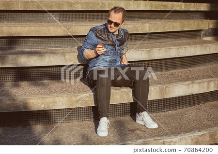 Russian man with smartphone sits on stairs. Russian man with smartphone sits on stairs. 70864200