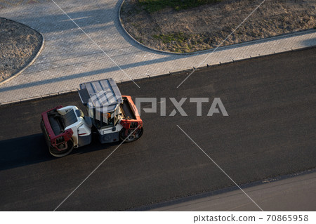 Asphalt road roller with heavy vibration roller compactor press new hot asphalt on the roadway on a road construction site. Heavy Vibration roller at asphalt pavement working. Repairing. 70865958