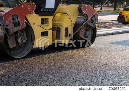 Asphalt road roller with heavy vibration roller compactor press new hot asphalt on the roadway on a road construction site. Heavy Vibration roller at asphalt pavement working. Repairing. 70865961