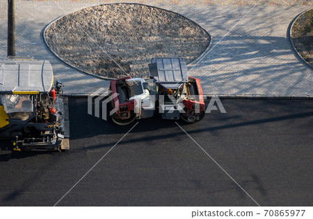 Industrial asphalt paver machine laying fresh asphalt and a Heavy road roller with vibration roller compactor press new hot asphalt on a road construction site. 70865977