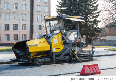 Industrial asphalt paver machine laying fresh asphalt on road construction site on the street. A Paver finisher placing a layer of a new hot asphalt on the roadway on a construction site. Repairing. 70866042