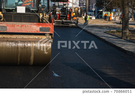 Asphalt road roller with heavy vibration roller compactor press new hot asphalt on the roadway on a road construction site. Heavy Vibration roller at asphalt pavement working. Repairing. Asphalt road roller with heavy vibration roller compactor press new hot asphalt on the roadway on a road construction site. Heavy Vibration roller at asphalt pavement working. Repairing. 70866051