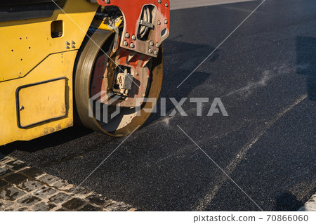 Asphalt road roller with heavy vibration roller compactor press new hot asphalt on the roadway on a road construction site. Heavy Vibration roller at asphalt pavement working. Repairing. 70866060
