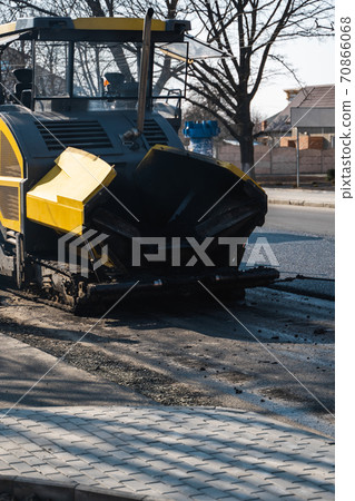 Industrial asphalt paver machine laying fresh asphalt on road construction site on the street. A Paver finisher placing a layer of a new hot asphalt on the roadway on a construction site. Repairing. 70866068
