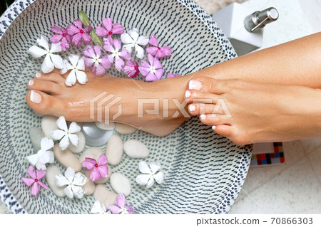 Spa treatment and product for woman feet and foot spa. Foot bath in bowl with tropical flowers, Thailand. Healthy Concept. Closeup  of  beautiful female feet, legs at spa salon on pedicure procedure. 70866303