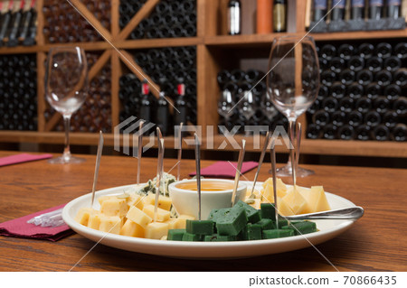 plate with appetizers for wine, several varieties of cheese and honey, on the background of shelving with wine 70866435
