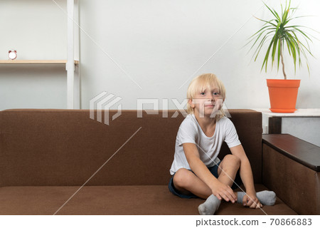 Smiling school-age boy sits on couch with his legs crossed. Free time for child 70866883